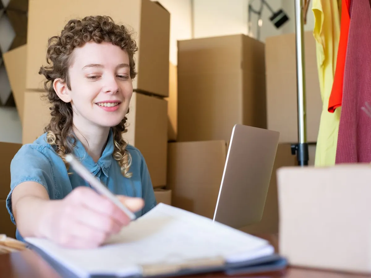 A small business owner writing notes beside packed boxes